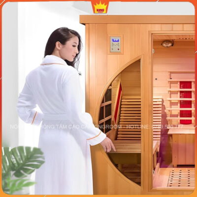 Người phụ nữ mặc áo choàng spa trắng đang mở cửa phòng xông hơi khô SM3 với thiết kế gỗ sang trọng