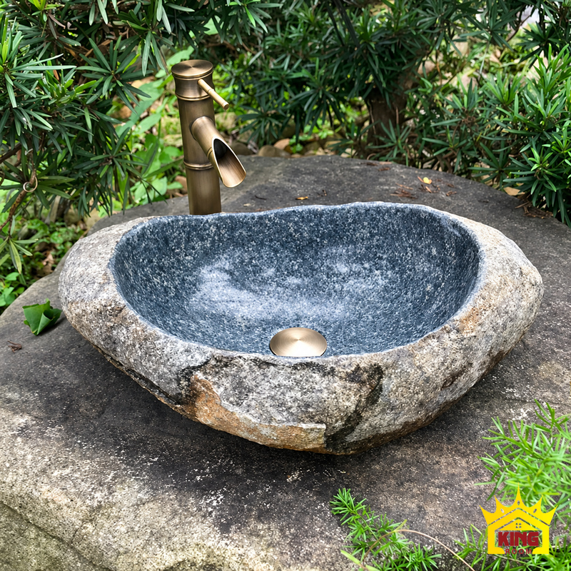 Chậu lavabo đá cuội tự nhiên đặt bàn lòng xám xanh, góc chính diện trên mặt kê đá xám, thành đá bất đối xứng, lòng xám xanh và nắp thoát nước kim loại
