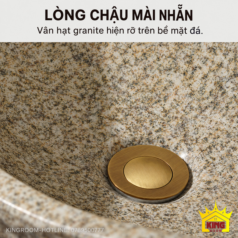 Cận cảnh lòng chậu lavabo đá cuội granite mài nhẵn, vân hạt xám be và nắp xả tông đồng