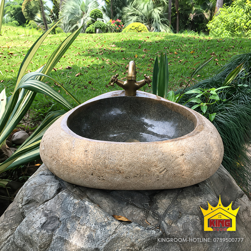 Chậu lavabo đá cuội tam giác bo góc, thành be mộc và lòng xám sẫm đặt trên mặt kê đá ngoài trời