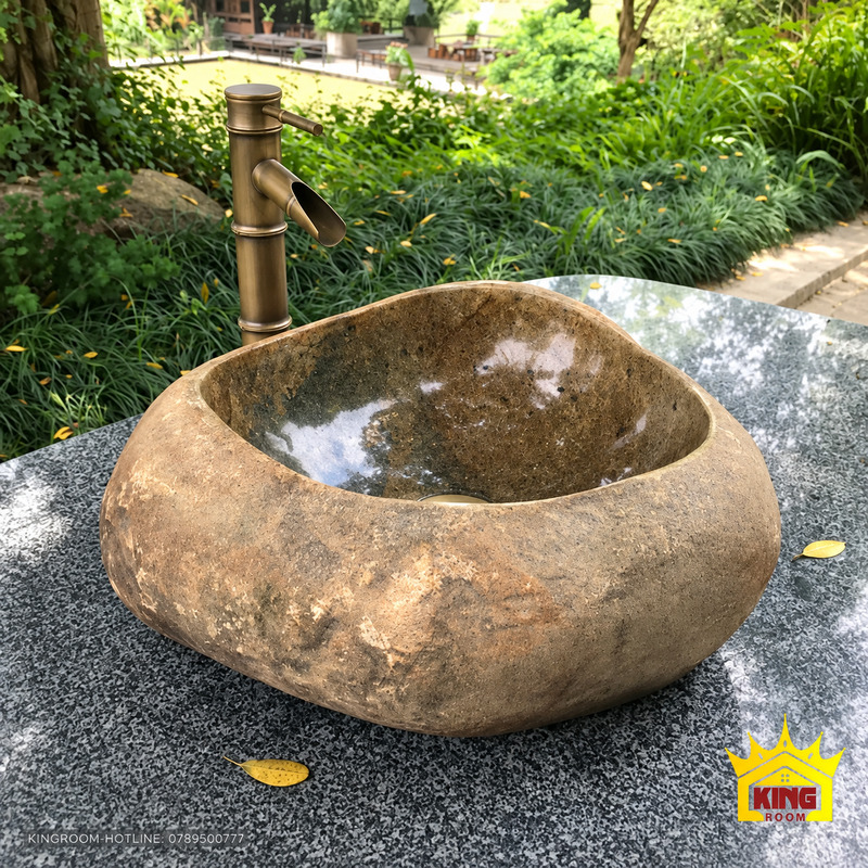 Chậu lavabo đá cuội tự nhiên nâu mộc đặt trên mặt bàn đá, lòng sẫm và vòi tông đồng cổ phía sau